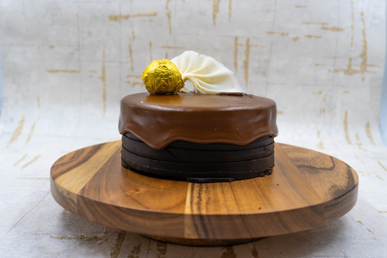 Artistic chocolate cake with gold and white decorations on a wooden stand, perfect for celebrations.