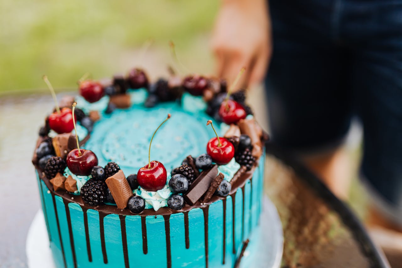 Close-up of a vibrant blue drip cake adorned with cherries, berries, and chocolate pieces.