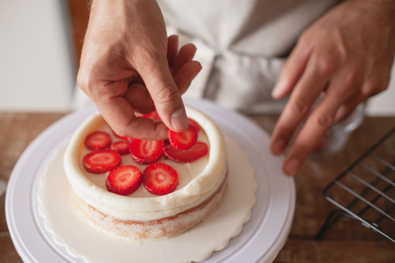 Close-up of a chef's hands artfully placing strawberry slices on a cake.
